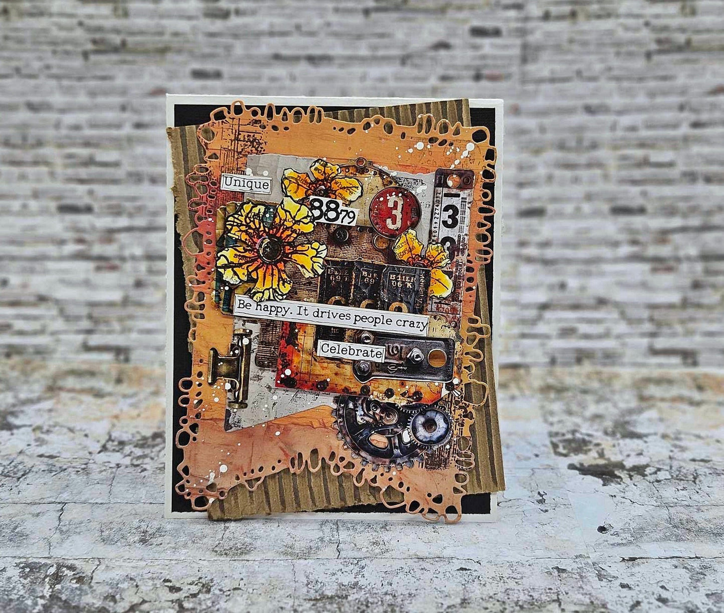 Steampunk card made with AALL & Create Bronze & Brassy Days papers featuring 'Be happy. It drives people crazy' and 'Celebrate' sentiments, yellow sunflowers, vintage numbers, gears, and distressed bronze and orange layered backgrounds