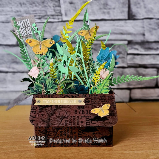 3D paper craft flower box sample using Arden Creative Studio Hidden Creek collection, featuring layered fern, grass and botanical die-cuts in teal and green, yellow butterfly die-cuts, blue paper flowers, and a "Together Forever / With Friends" sentiment on a dark vintage typography patterned box base.