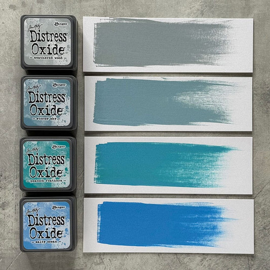 Four Ranger Distress Oxide ink pads from Kit 4 with swatched colours: Weathered Wood, Stormy Sky, Peacock Feathers and Salty Ocean, shown on white paper beside each labelled pad.