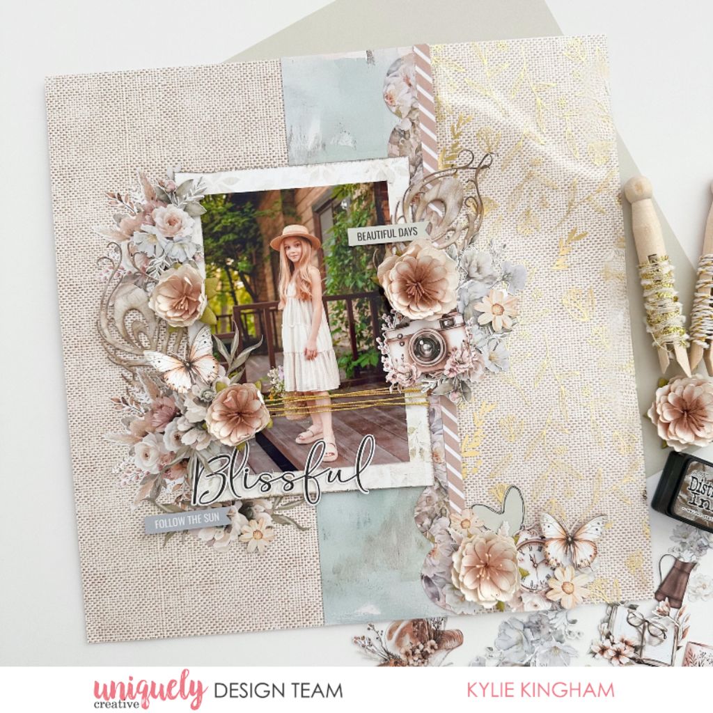 Scrapbook page by Kylie Kingham using Uniquely Creative Bohemian Escape collection – features a central photo framed by pastel florals, butterflies, vintage camera, and layered embellishments. Sentiments like “Blissful” and “Follow the Sun” enhance the soft, nature-inspired design perfect for documenting beautiful days.