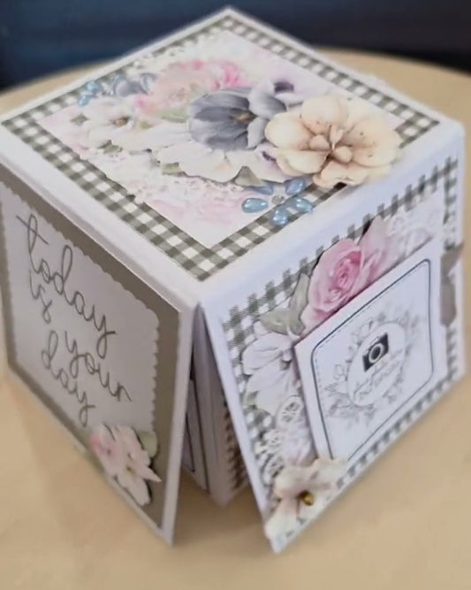 White memory box folio decorated with soft floral papers, dimensional flowers, and gingham trim, featuring 'today is your day' sentiment and photo mats on each side