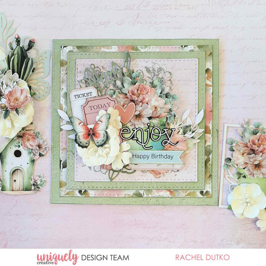 Tea and Tranquility handmade card by Uniquely Creative design team — layered square "Enjoy Happy Birthday" card featuring lush floral clusters, butterfly and ticket die-cuts, and a heart embellishment in soft sage, blush, and cream