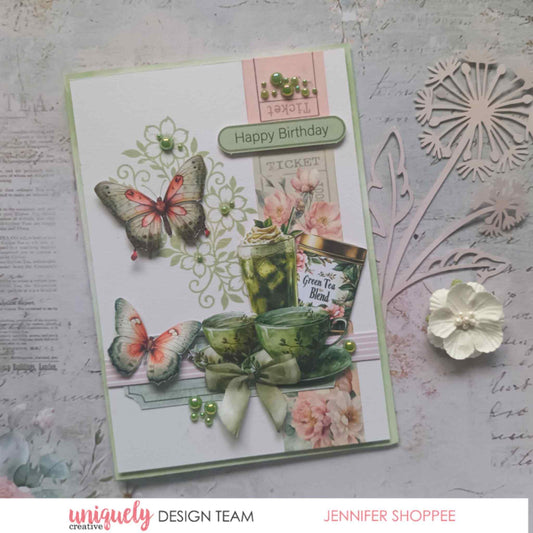 Tea and Tranquility handmade card by Uniquely Creative design team — "Happy Birthday" card featuring green tea cup and tin die-cuts, butterfly embellishments, ticket strip, stamped floral swirl, and green pearl accents on a soft sage and blush background