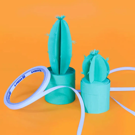 Two paper cacti in teal cardstock with a roll of X-Press It Tape draped around showing you can use this tape for many craft projects.