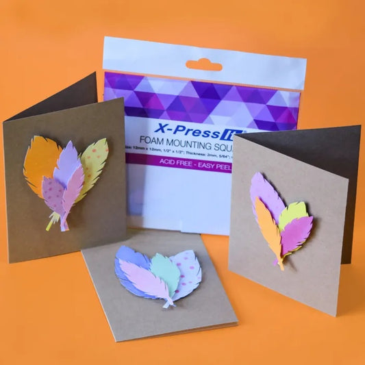 Colourful feather designs mounted on brown cards with X-Press It 12mm foam mounting squares in the background.