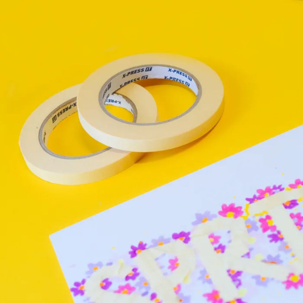 Two rolls of masking tape on a yellow background with a piece of paper featuring colourful designs showing how they have masked off an area to decorate around it.