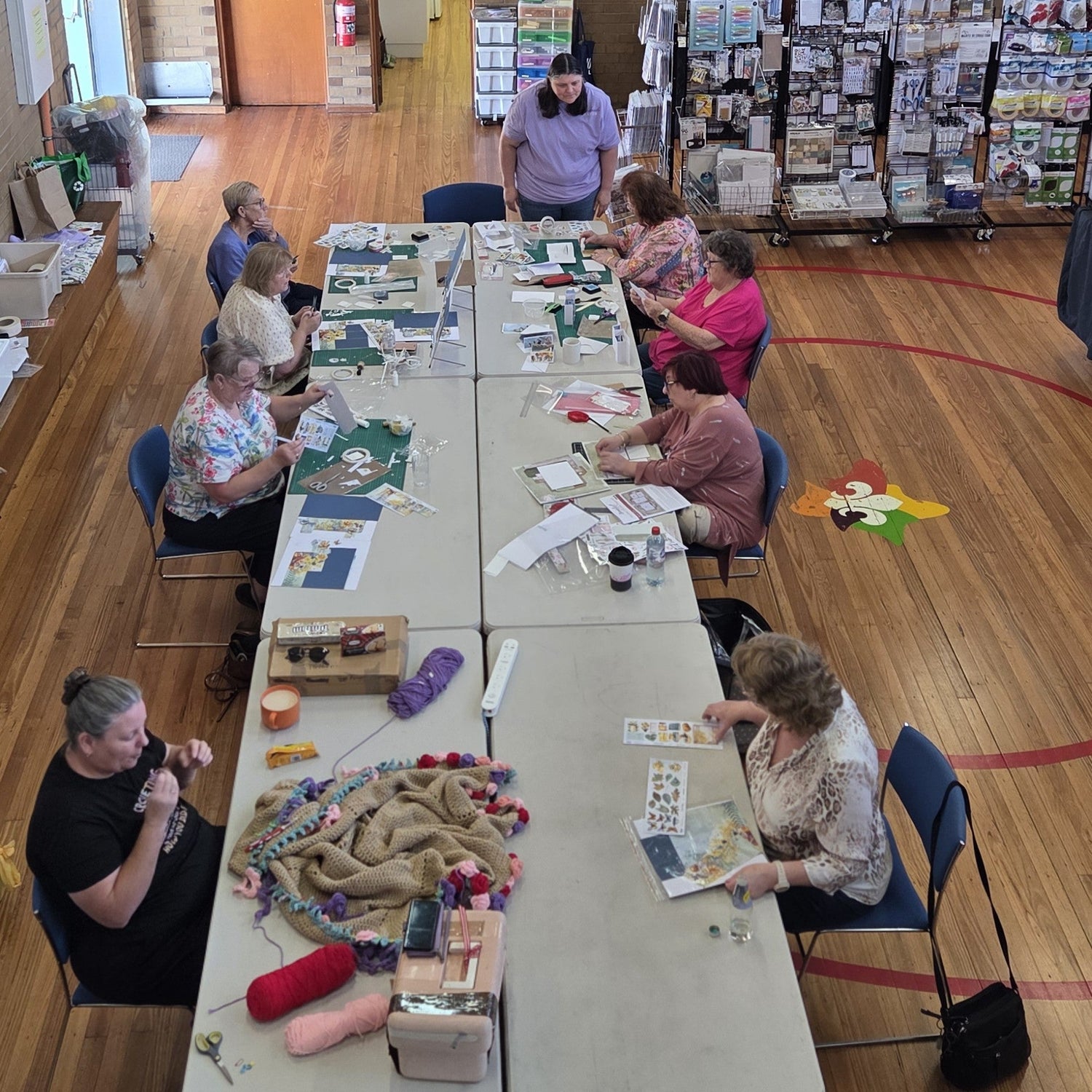 A group of ladies sitting at tables scrapbooking and crocheting. Some are participating in a card making class. 