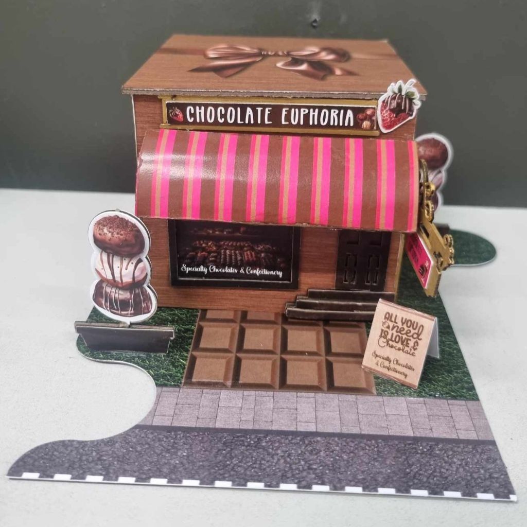 Assembled Chocolate Euphoria miniature shop with pink and brown striped awning, chocolate bar footpath, and copper bow on the rooftop