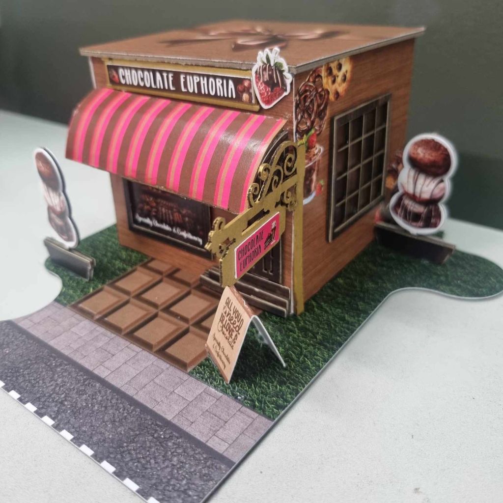 Side angle of the Chocolate Euphoria shop showing the ornate gold scrollwork door surround and die-cut chocolate truffle characters