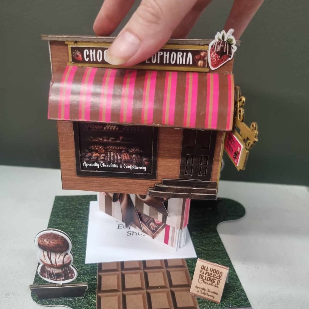 Chocolate Euphoria miniature building being lifted to reveal the mini album tucked inside