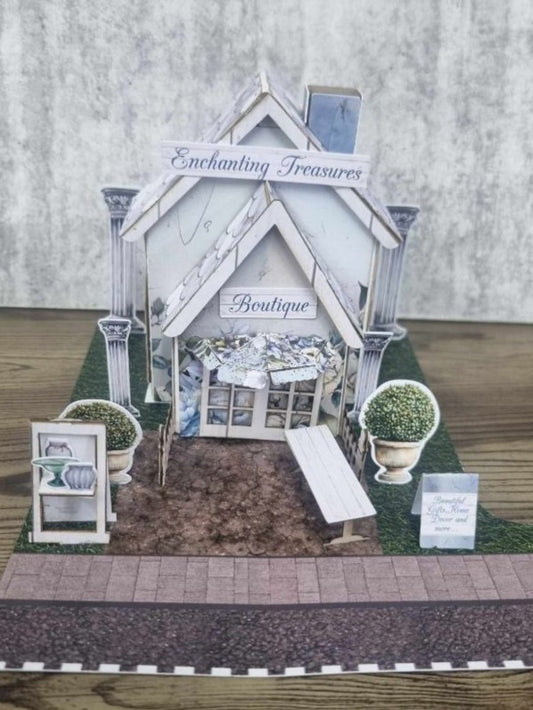 3Quarter Designs Enchanting Treasures Boutique Gift Shop miniature building front view showing white facade with Enchanting Treasures sign, Boutique entrance, ornate columns, topiary urns, picket fence, and cobblestone path