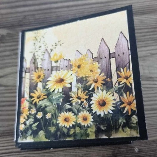 Mini album closed, front cover showing sunflowers and picket fence illustration with black binding
