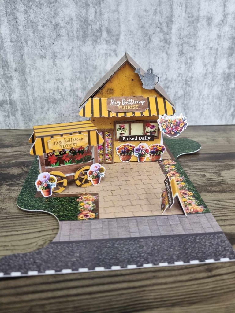 Front view of Hey Buttercup Florist showing the Picked Daily sign, hanging basket die-cuts, potted flower embellishments, and A-frame sandwich board