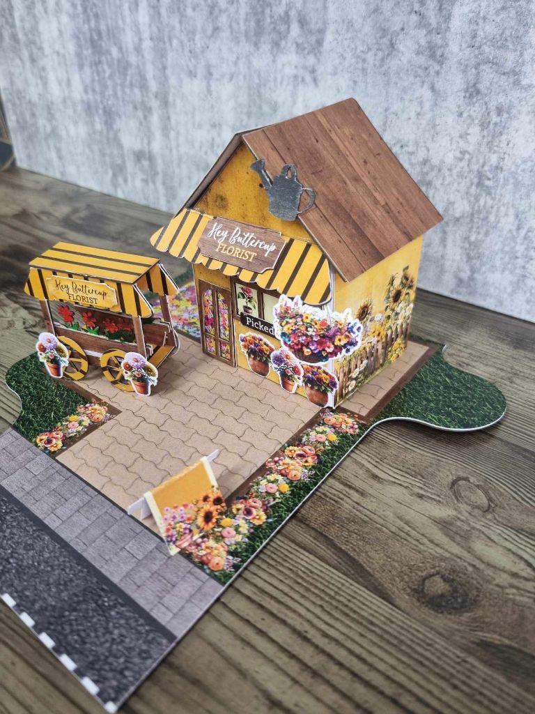 Side view of Hey Buttercup Florist showing the sunflower garden bed, picket fence, and entrance detail