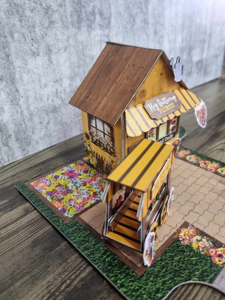Side angle of Hey Buttercup Florist showing the sunflower wall mural, flower cart, and jigsaw-shaped base board with road section