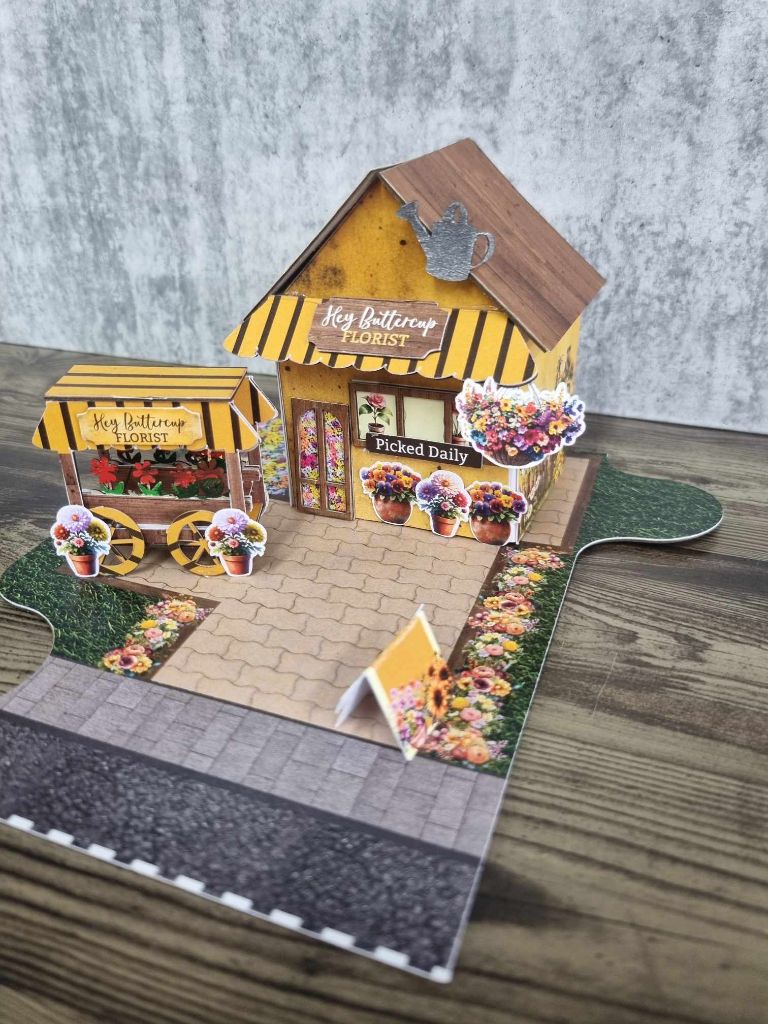 Wide view of Hey Buttercup Florist showing the complete scene with flower cart, sunflower garden, cobblestone path, and jigsaw base board 