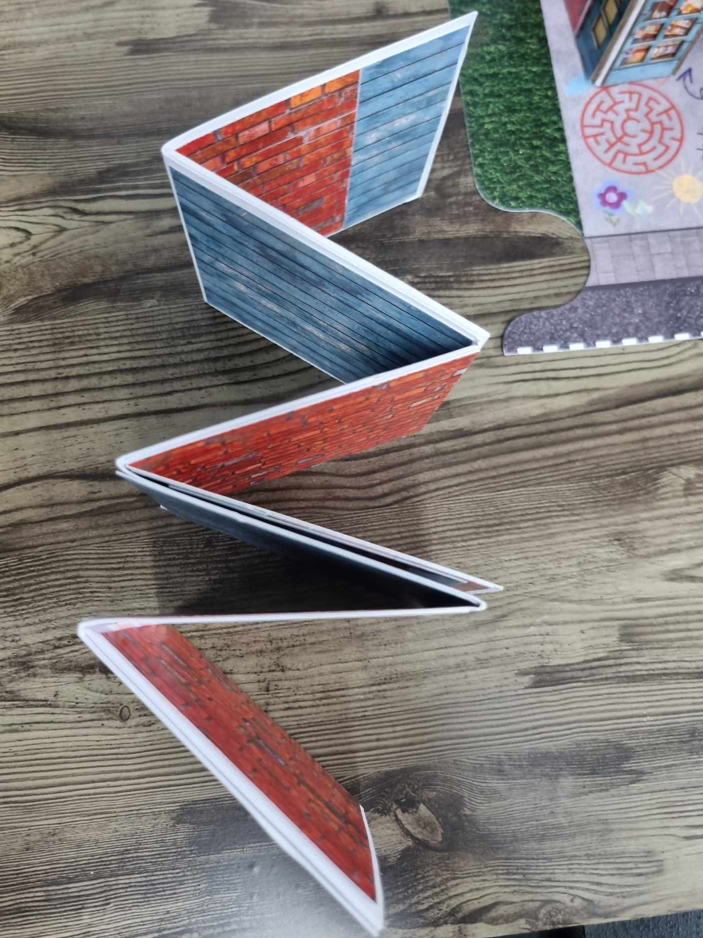  3Quarter Designs Little Wonders Toy Emporium mini album standing upright in concertina formation showing alternating red brick and blue timber-look accordion pages, with assembled toy shop base board visible in background