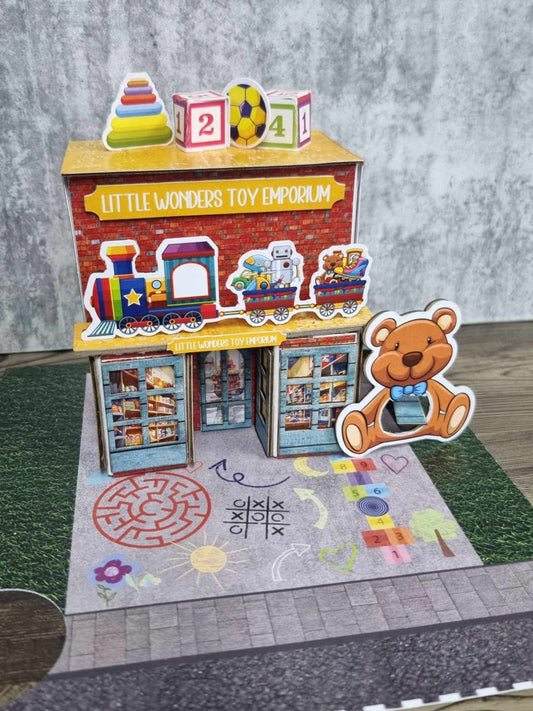 3Quarter Designs Little Wonders Toy Emporium front view showing toy train awning, number block and soccer ball rooftop details, and chalk-art playground base board
