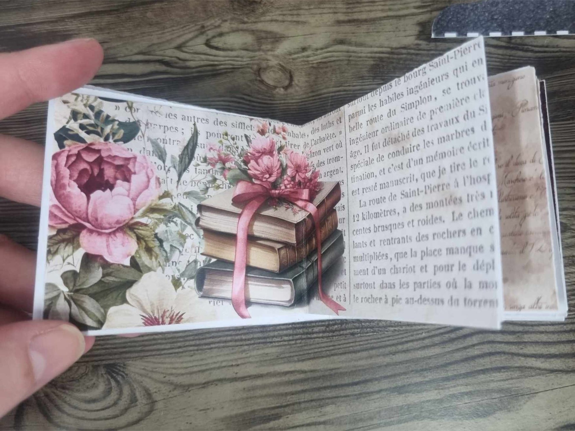 3Quarter Designs Once Upon a Time Book Shop mini album open showing an interior spread with a stack of ribbon-tied vintage books and pink peonies on an aged French script background, with a handwritten script journaling page on the right