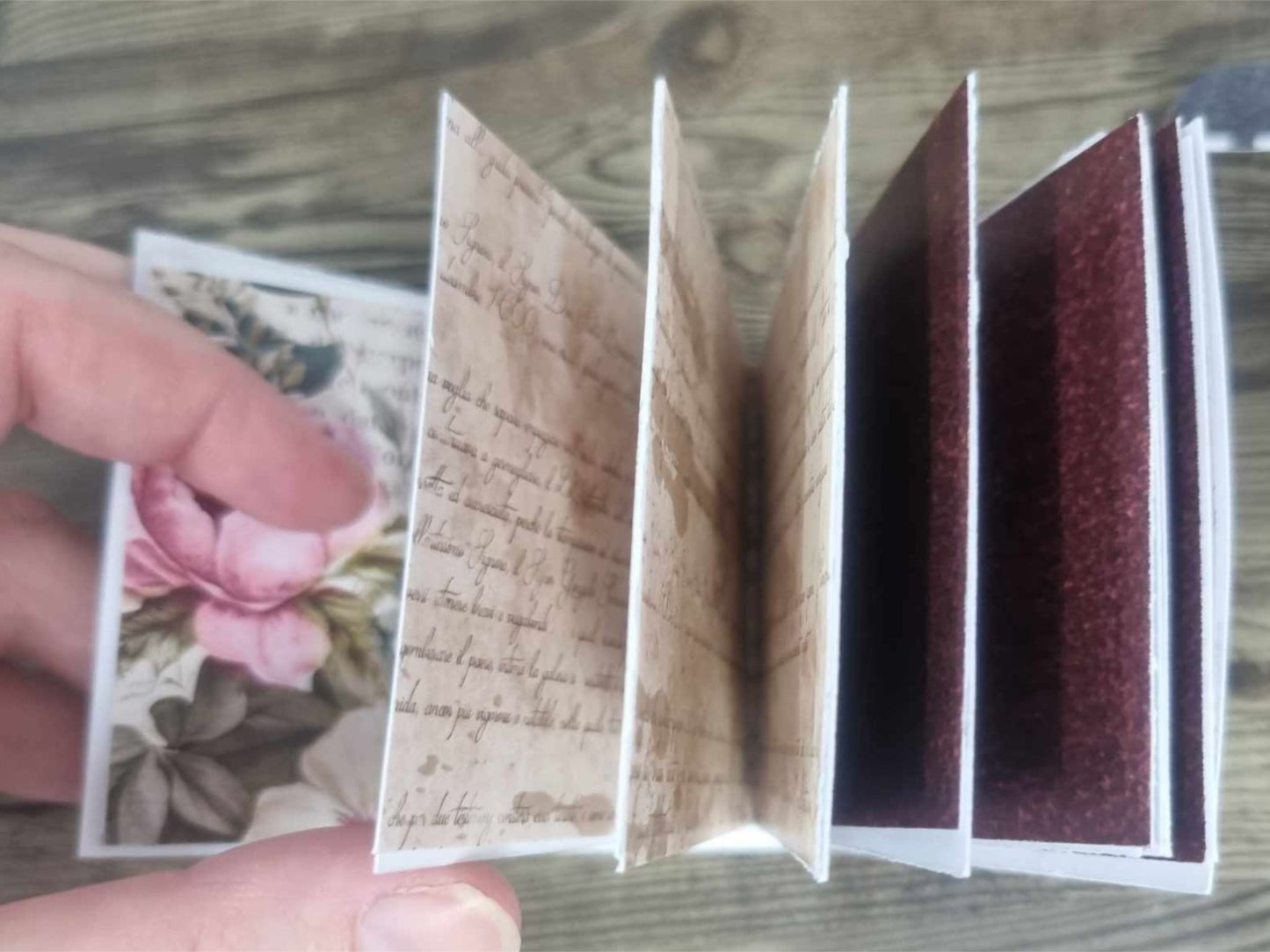 3Quarter Designs Once Upon a Time Book Shop mini album held open showing alternating pages of aged French script journaling paper and dark burgundy pages, with a pink peony and botanical floral page visible on the left