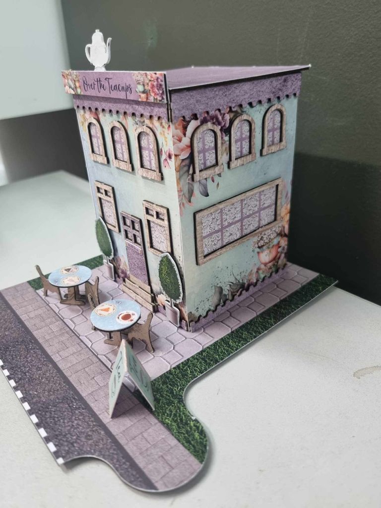 Side angle of the Over the Teacups Café miniature building showing the jigsaw-shaped base board