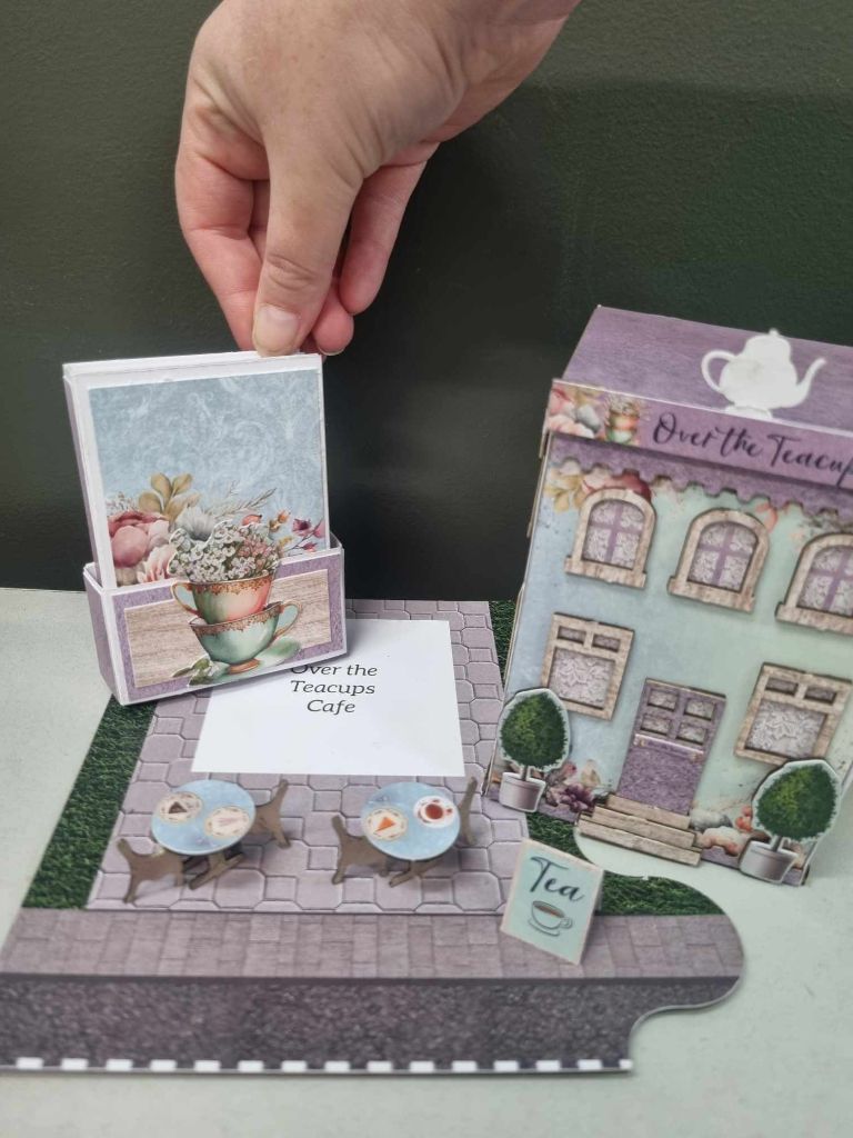 Mini album being placed inside the Over the Teacups Café, showing how the included A4 papers can be used