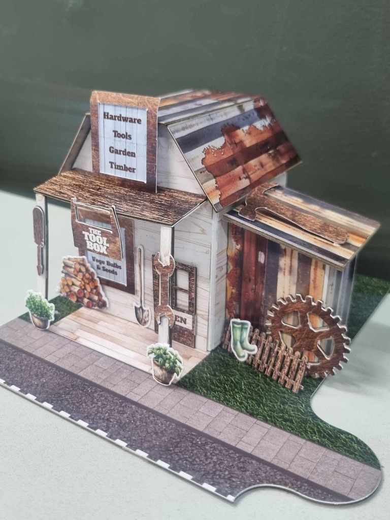 Angled view of The Toolbox showing the rustic lean-to shed, cog wheel, gumboots, and picket fence