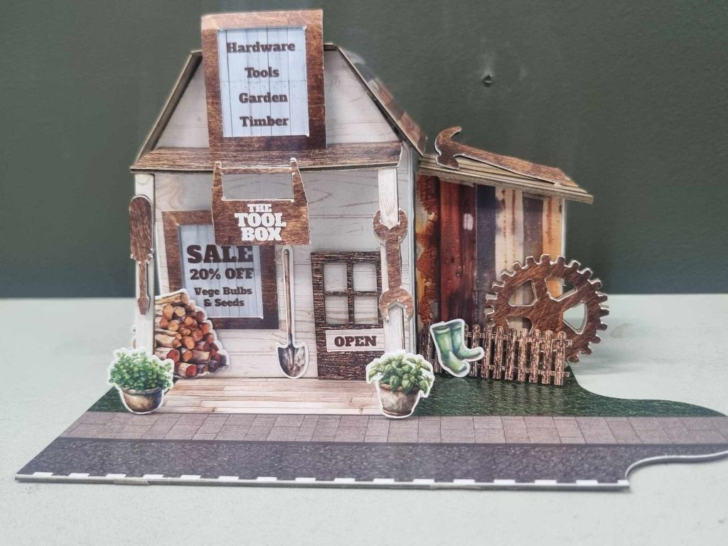 Front view of The Toolbox showing the sale window sign, garden tools, firewood stack, and Open sign