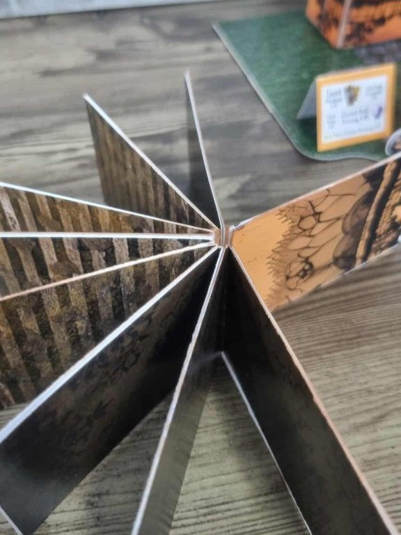 3Quarter Designs Witchwood Charm Tarot Store hidden star book viewed from the spine showing all pages fanned out in a full star shape, with alternating dark gothic timber and aged orange Halloween pages radiating from the central binding