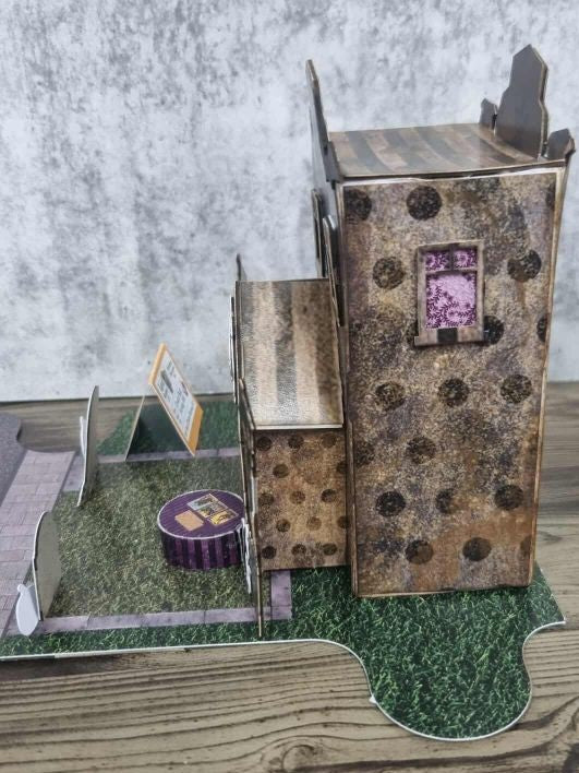 3Quarter Designs Witchwood Charm Tarot Store miniature building right side view showing dark textured spotty gothic paper walls, striped timber porch roof extension, purple lace framed upper window, purple striped crystal ball table, and grass jigsaw base board with cobblestone road section