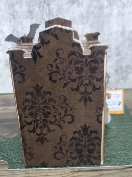 3Quarter Designs Witchwood Charm Tarot Store miniature building rear view showing dark gothic damask wallpaper panels covering the full back wall, ornate battlement roofline with bat die-cuts, exposed chipboard edges, and grass graveyard base board