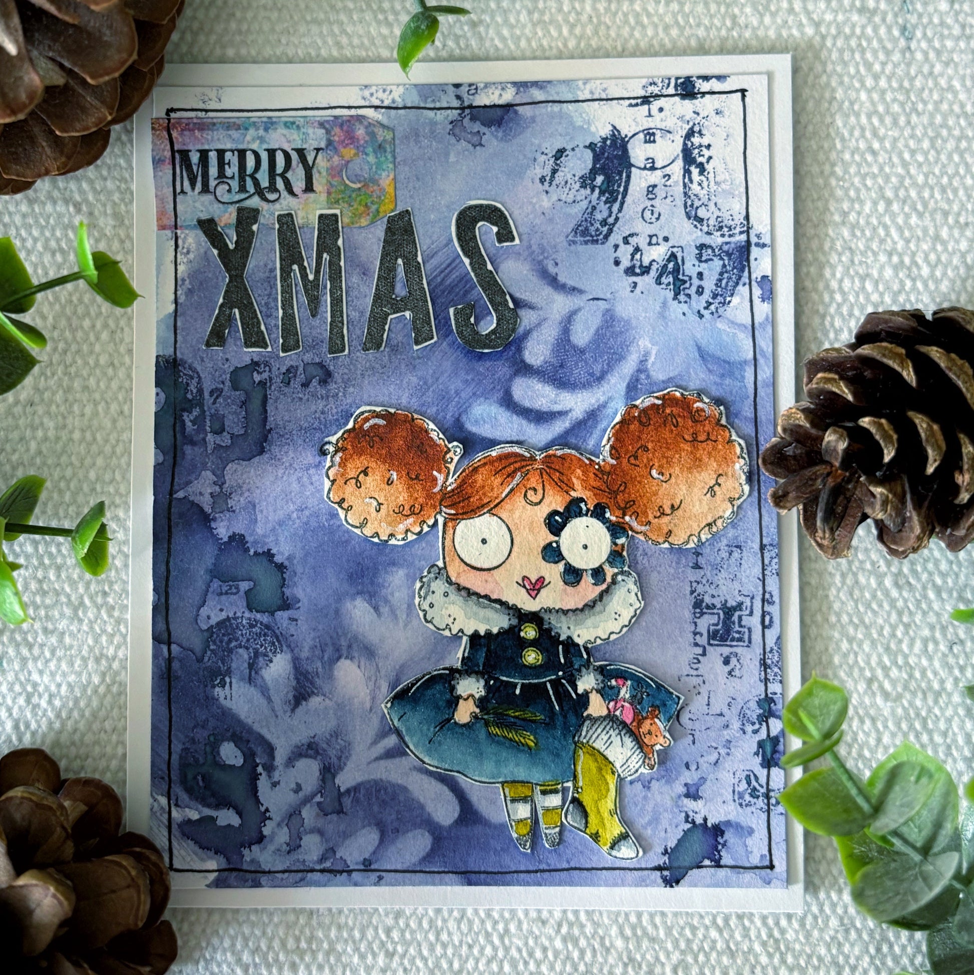 Mixed media Christmas card using AALL & Create number and symbol stamps creating 'XMAS' with blue watercolour background, and a cartoon styled girl with red hair. 