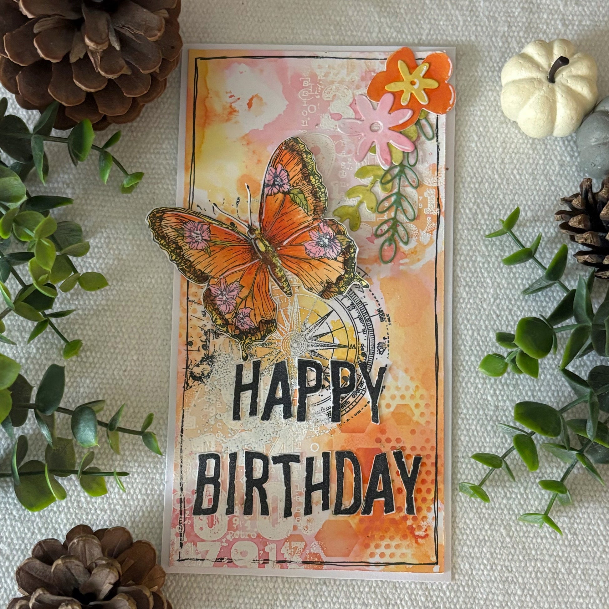 Happy Birthday card made with AALL & Create alphabet stamps featuring orange butterfly, die-cut flowers, compass imagery, and mixed media background in warm autumn tones
