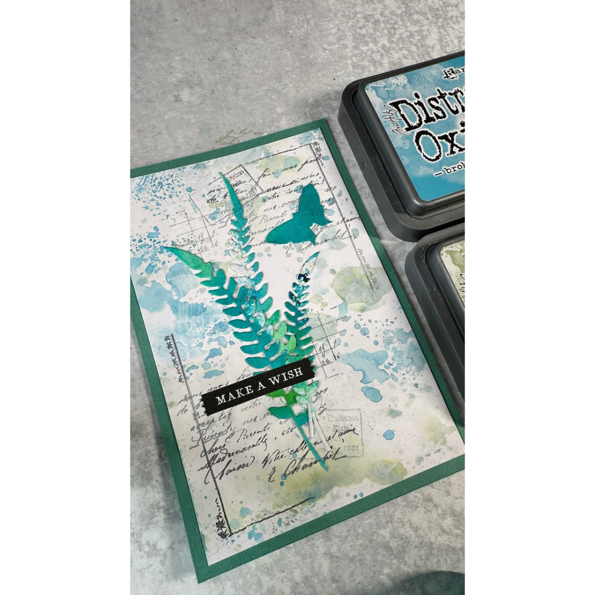 Handmade card sample using Arden Creative Studio Hidden Creek collection, featuring teal die-cut ferns, butterfly embellishment, and Distress Oxide ink blending on a vintage script background.