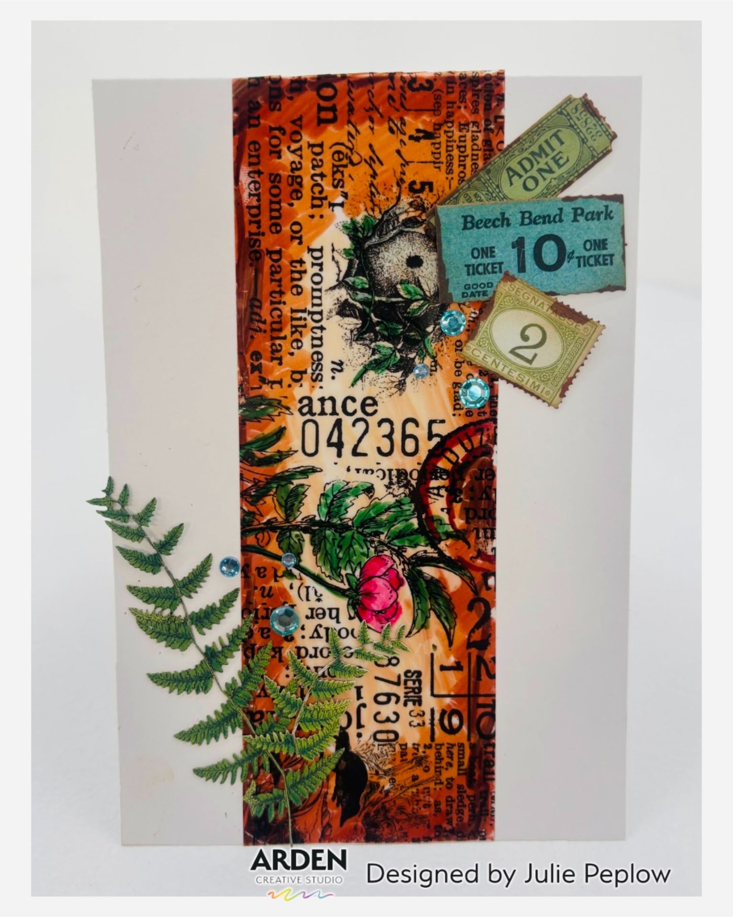 Handmade card sample using Arden Creative Studio Hidden Creek collection, featuring warm orange mixed media background with vintage typography stamping, botanical rose and bird's nest stamping, die-cut fern embellishment, teal rhinestone accents, and layered vintage ticket ephemera.
