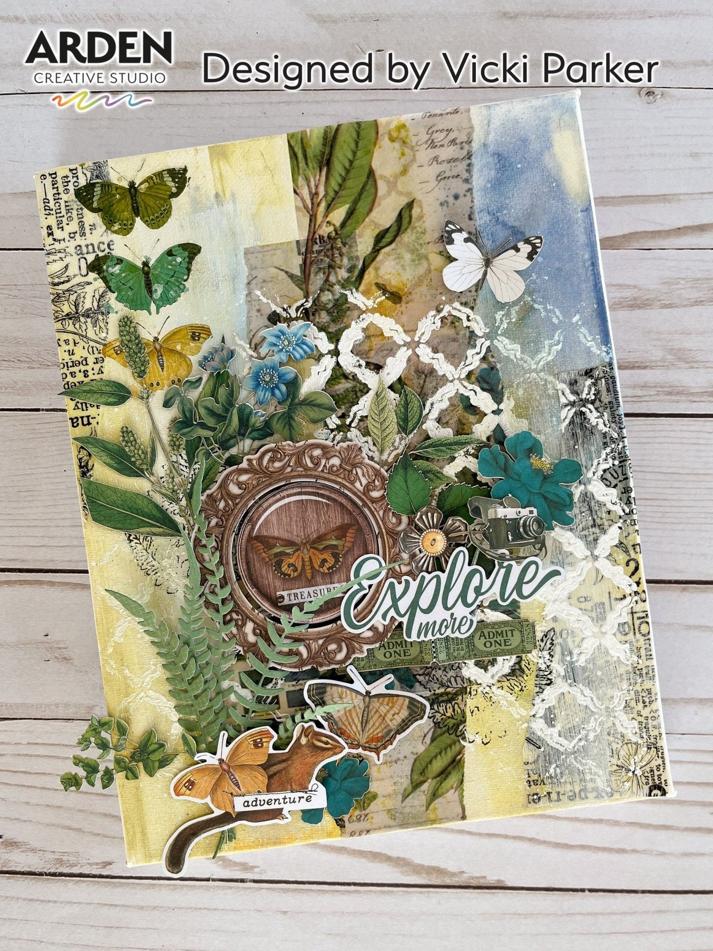 Mixed media art journal page sample using Arden Creative Studio Hidden Creek collection, featuring layered botanical die-cuts in green and teal, multiple butterfly die-cuts, squirrel die-cut, vintage map and compass embellishments, ornate mirror frame focal point, ticket ephemera, and "Explore More / Adventure" sentiments.