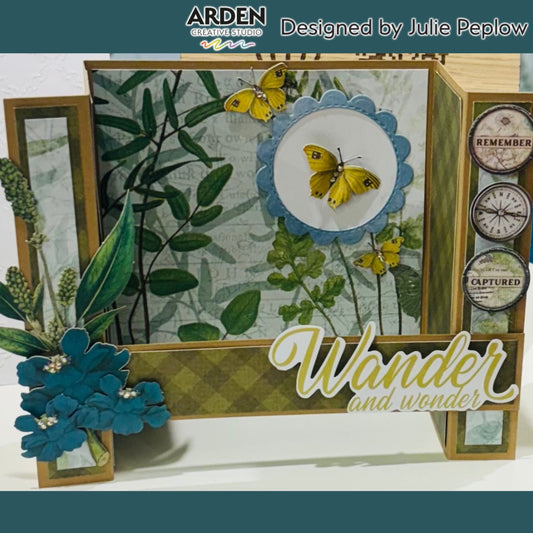 Handmade "Wander and Wonder" easel card sample using Arden Creative Studio Hidden Creek collection, featuring botanical leaf patterned paper, yellow butterfly die-cuts in a scalloped circle frame, teal paper flower cluster with rhinestone centres, compass and map circle embellishments, and gold diamond patterned cardstock.