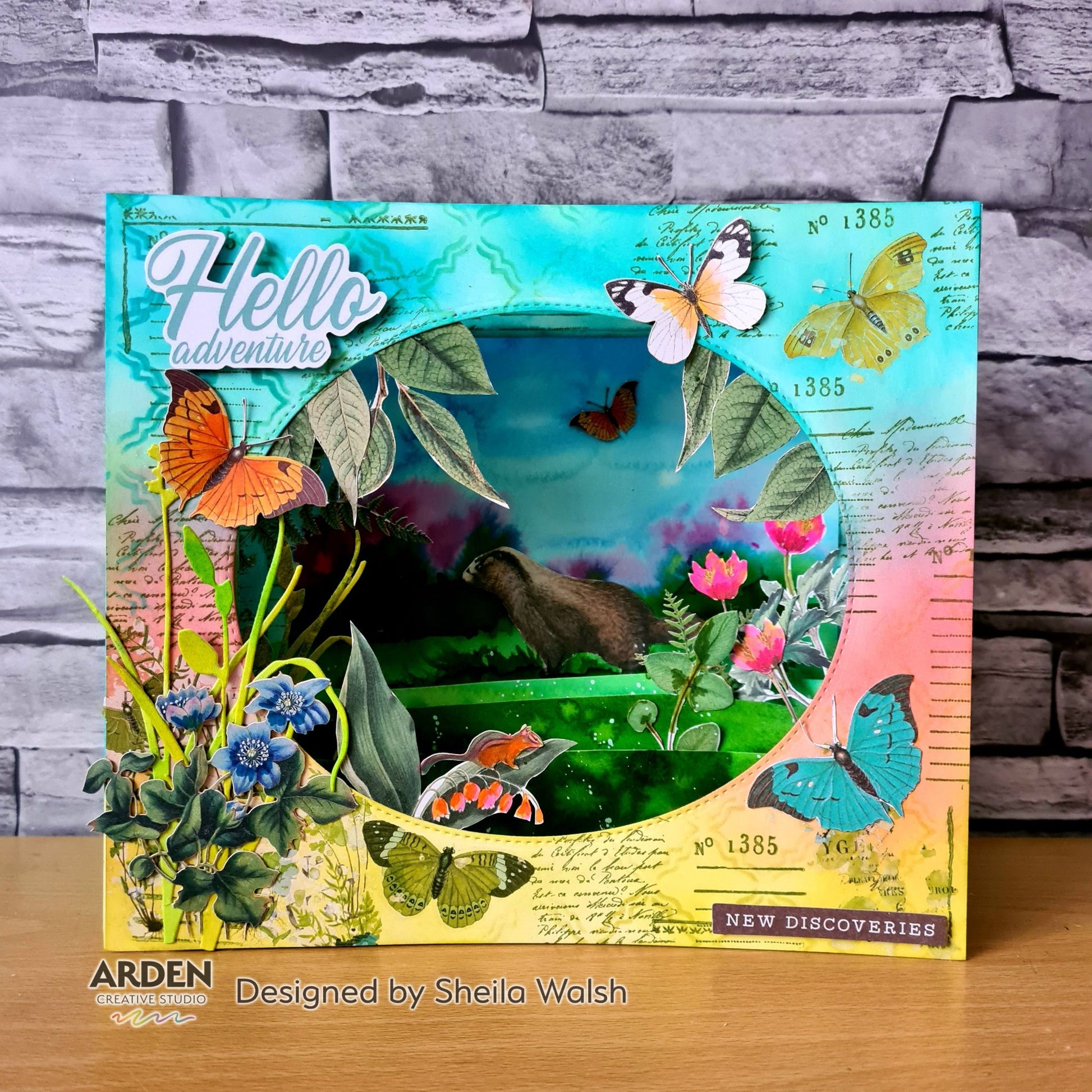 3D shadow box card sample using Arden Creative Studio Hidden Creek collection, featuring vibrant teal and yellow ink blending, multiple butterfly die-cuts in orange, teal and yellow, botanical leaf die-cuts, blue floral embellishments, chipmunk die-cut, and "Hello Adventure / New Discoveries" sentiments.