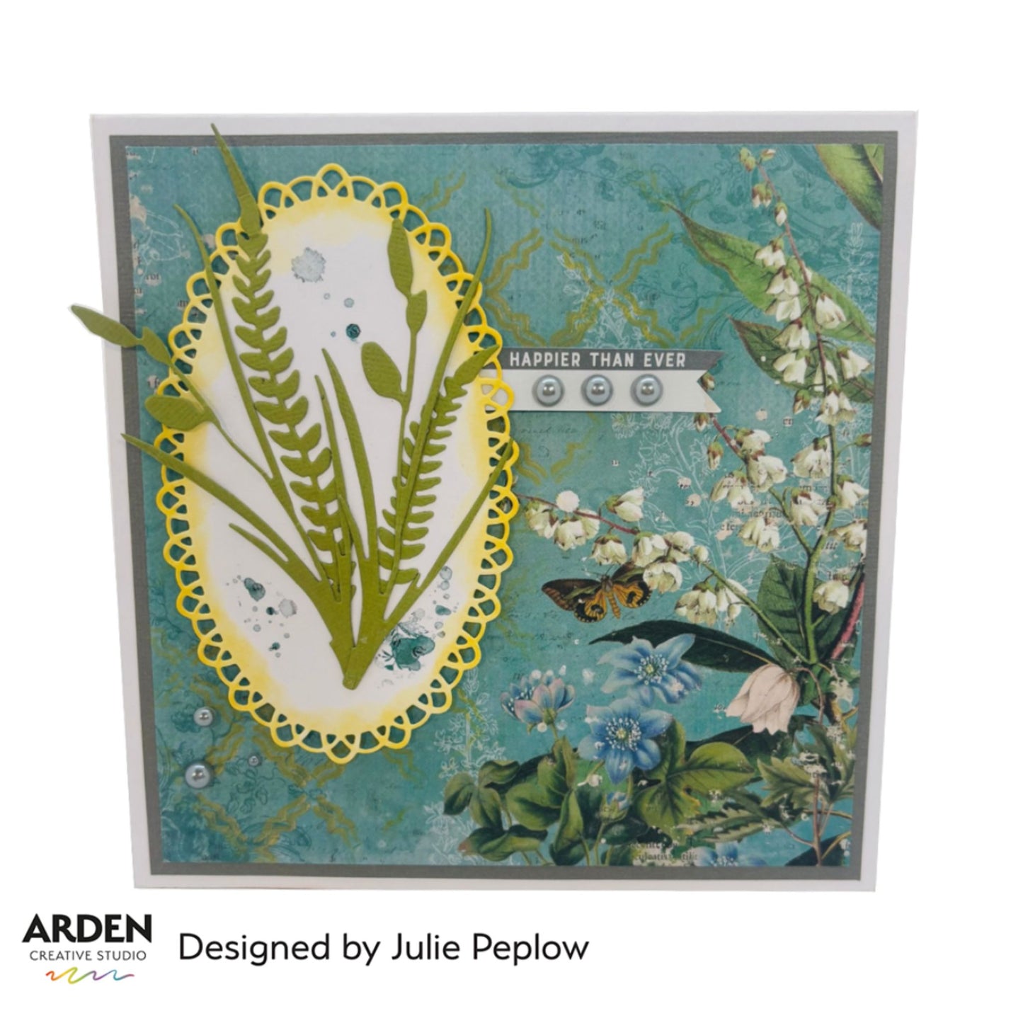 Handmade "Happier Than Ever" card sample using Arden Creative Studio Hidden Creek collection, featuring a yellow lace oval die-cut frame with botanical fern die-cuts on a white ink-splattered panel, layered over a teal floral and lily of the valley patterned paper background with butterfly and pearl embellishments.