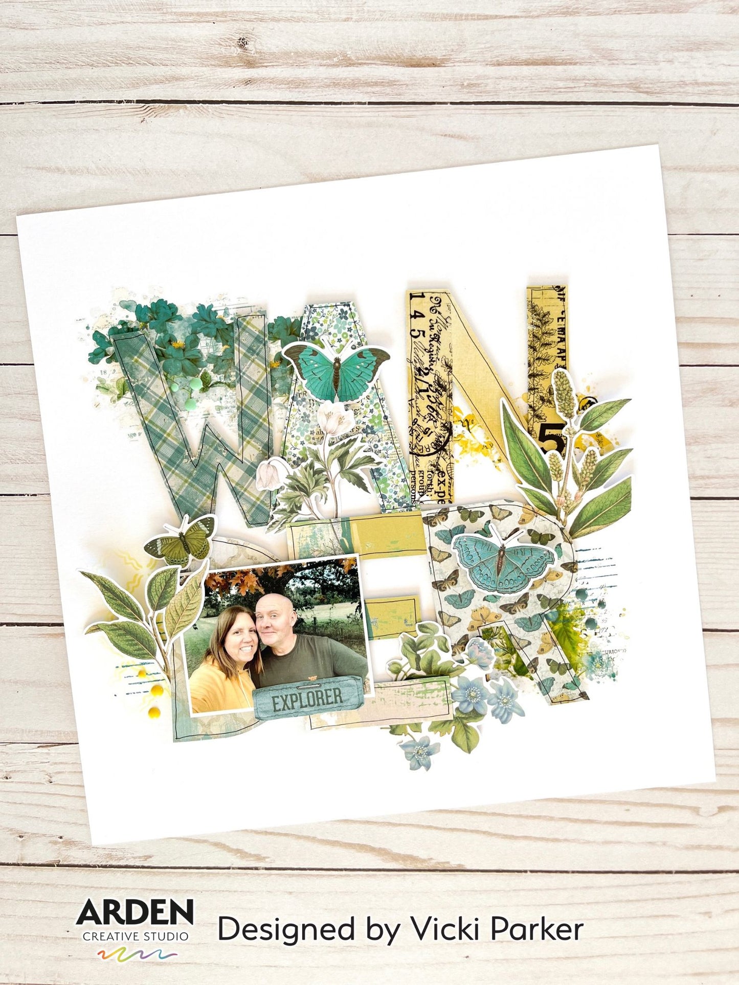 "Wander" scrapbook layout sample using Arden Creative Studio Hidden Creek collection, featuring large patterned paper alphabet letters, botanical leaf and butterfly die-cuts, and vintage typography ephemera on a white background.