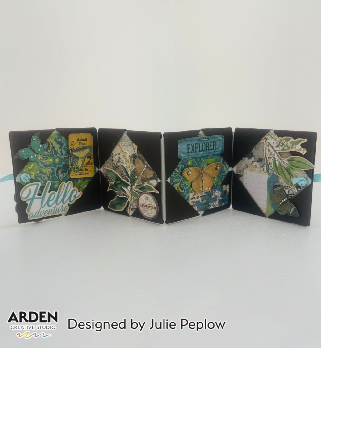 "Hello Adventure / Explorer" accordion fold mini album sample using Arden Creative Studio Hidden Creek collection, featuring four diamond-shaped panels on a black base with botanical die-cuts, butterfly embellishments, teal floral clusters, and vintage ticket ephemera.