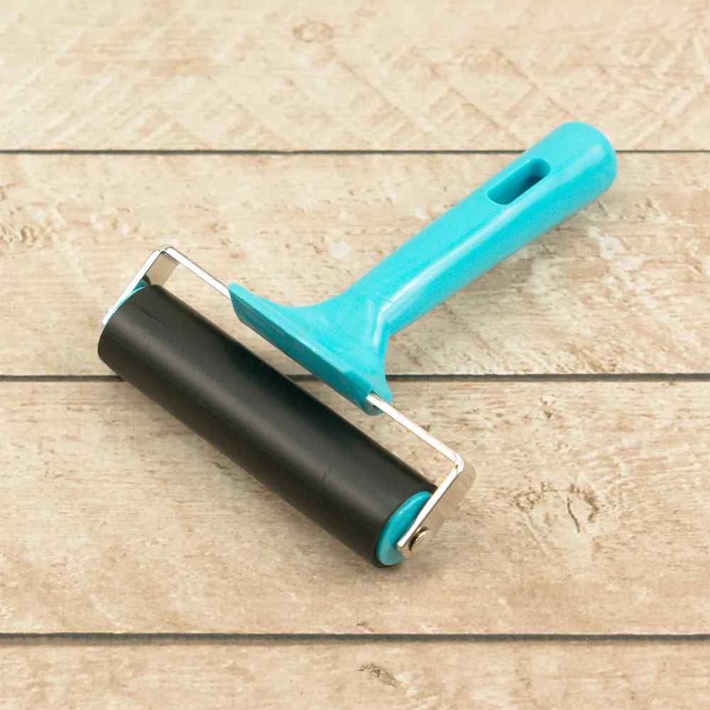 Couture Creations 100mm brayer with black rubber roller and turquoise handle on a wood surface