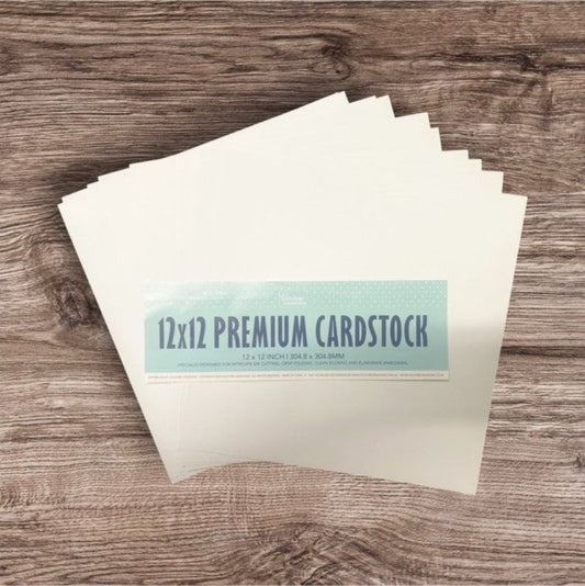 Stack of 12x12 premium white 216gsm cardstock sheets on a wooden surface