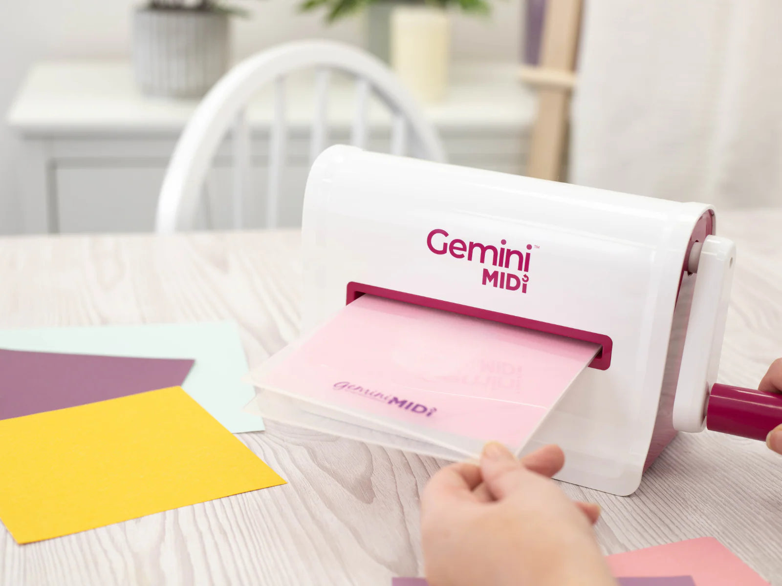 Gemini Midi die cutting machine in use with plastic folder feeding pink cardstock through rollers