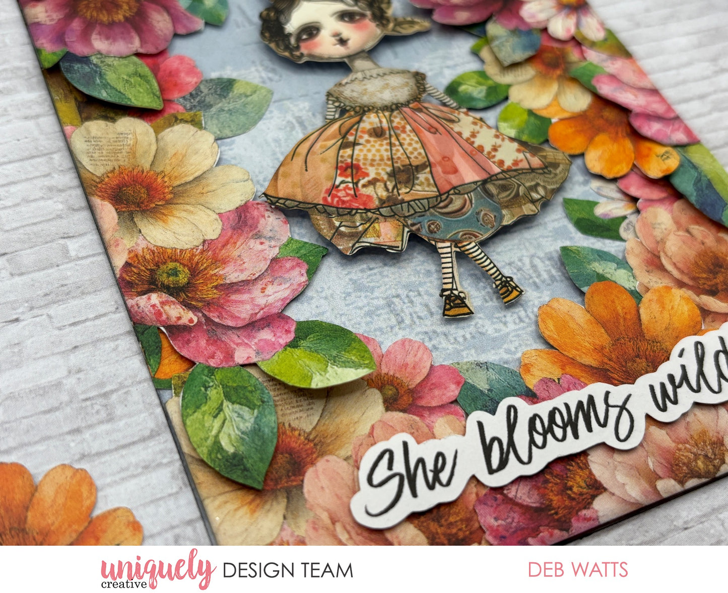 Mixed media project using Uniquely Creative Dressed in Daydreams collection featuring whimsical girl die-cut with striped stockings, layered watercolour flowers in pink and orange, and 'She blooms wild' sentiment