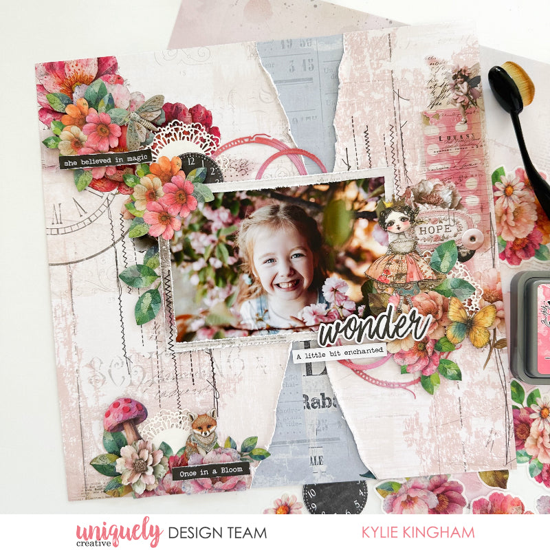 Mixed media scrapbook page featuring Uniquely Creative Dressed in Daydreams vintage ephemera, watercolour florals in pink and coral, mushroom embellishment, lace doily, 'she believed in magic' and 'wonder' sentiments on distressed background