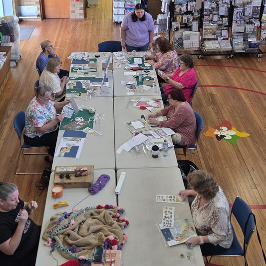 Group of crafters sitting around tables at a paper crafting workshop event, working on scrapbooking and card making projects with die-cuts and embellishments
