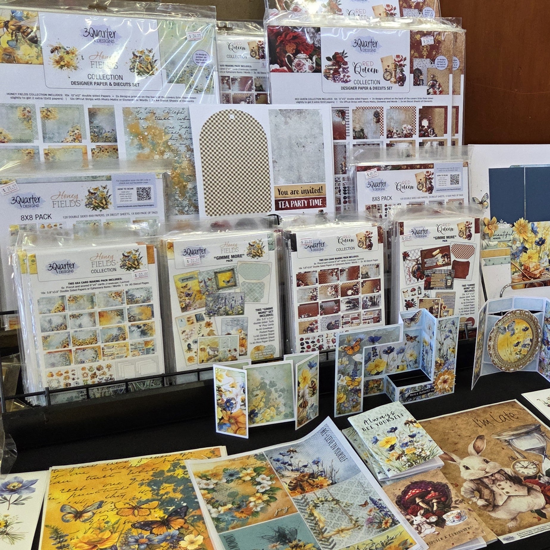 Display of 3Quarter Designs Honey Fields and Queen collections featuring designer paper packs, die-cuts, and coordinating embellishments at craft event