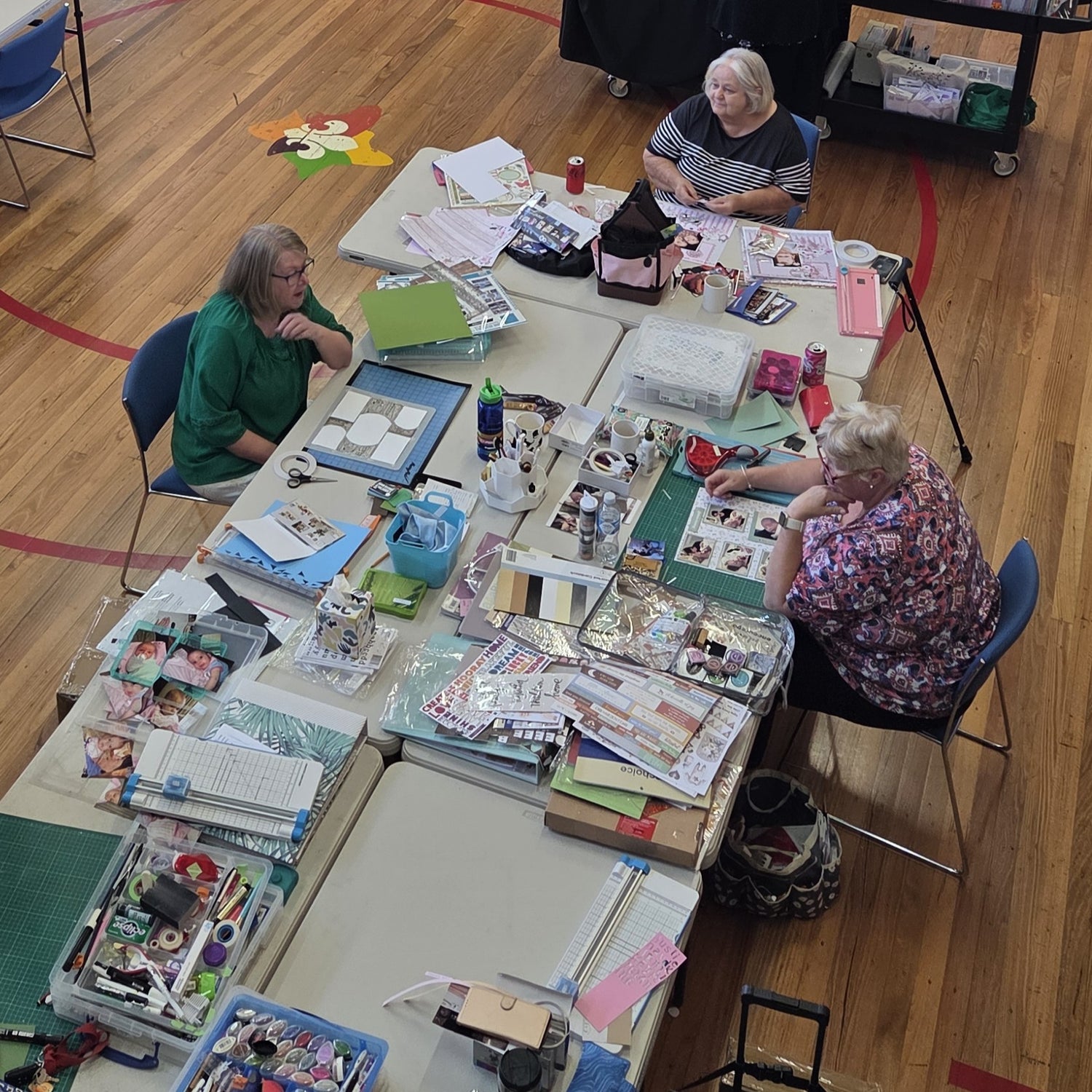Three crafters working on scrapbooking projects with supplies spread across tables at Handmade Haven Crop & Craft Day in Morwell