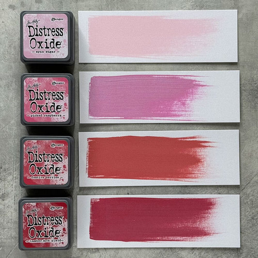 Four Ranger Distress Oxide ink pads from Kit 1 with swatched colours: Spun Sugar, Picked Raspberry, Festive Berries and Lumberjack Plaid, shown on white paper beside each labelled pad.
